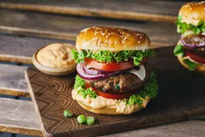 Two burgers on a wooden cutting board with a side of dipping sauce