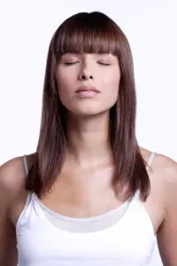 Woman with her eyes closed and her head in her hands, wearing a white tank top against a white background