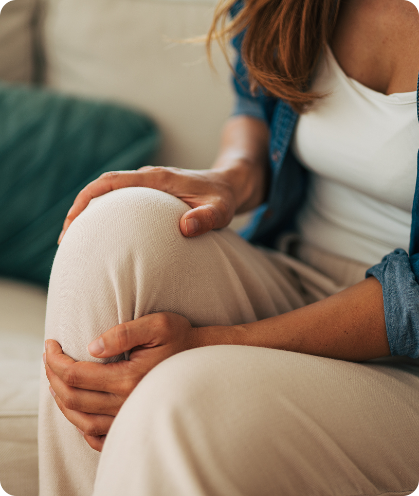 Woman sitting on a couch, holding her knee in pain