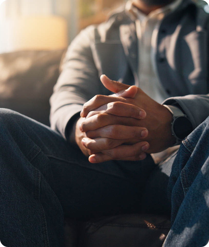 Man sitting on a couch with his hands clasped together, wearing a watch