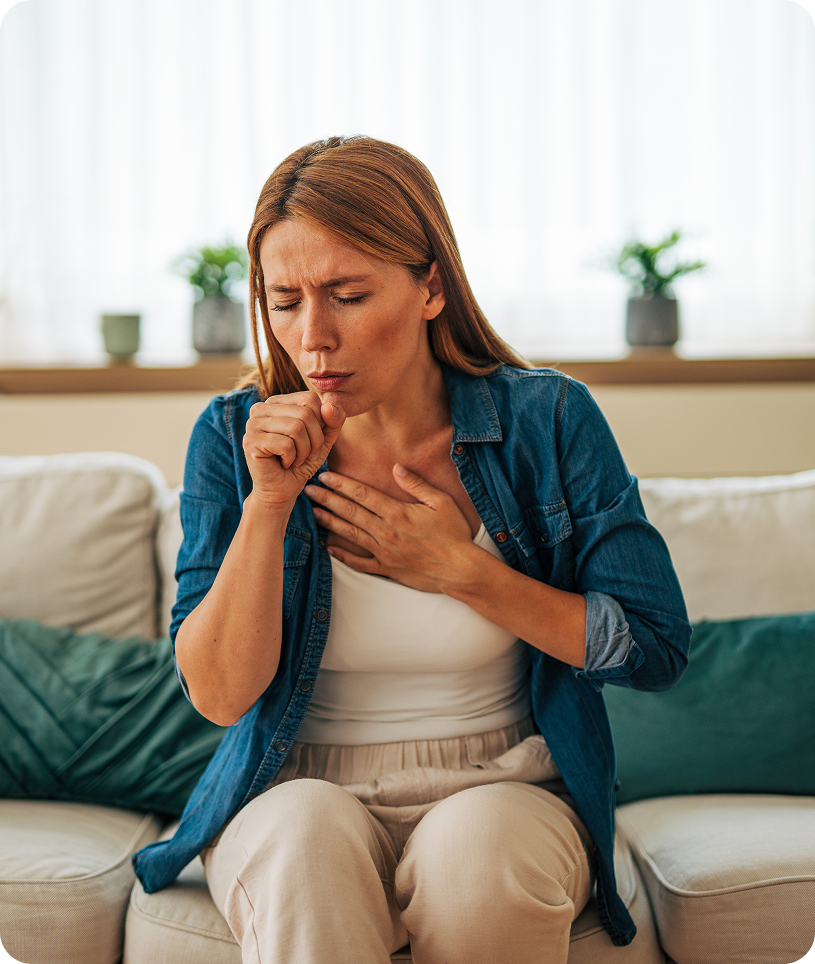Woman sitting on a couch with her chest in pain, surrounded by cushions and a blanket