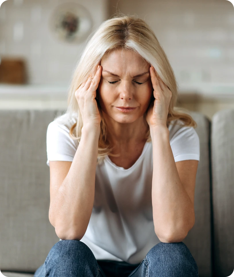 Woman sitting on a couch with her head in her hands, wearing a t-shirt and jeans