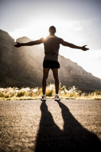 Rear view of a male athlete with his arms outstretched, looking out over a mountain